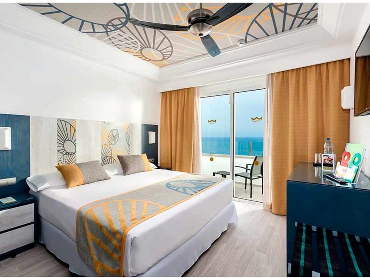 A bright double room with a sea-view balcony, a large bed, a small sofa and RIU's crown-motif soft furnishings.