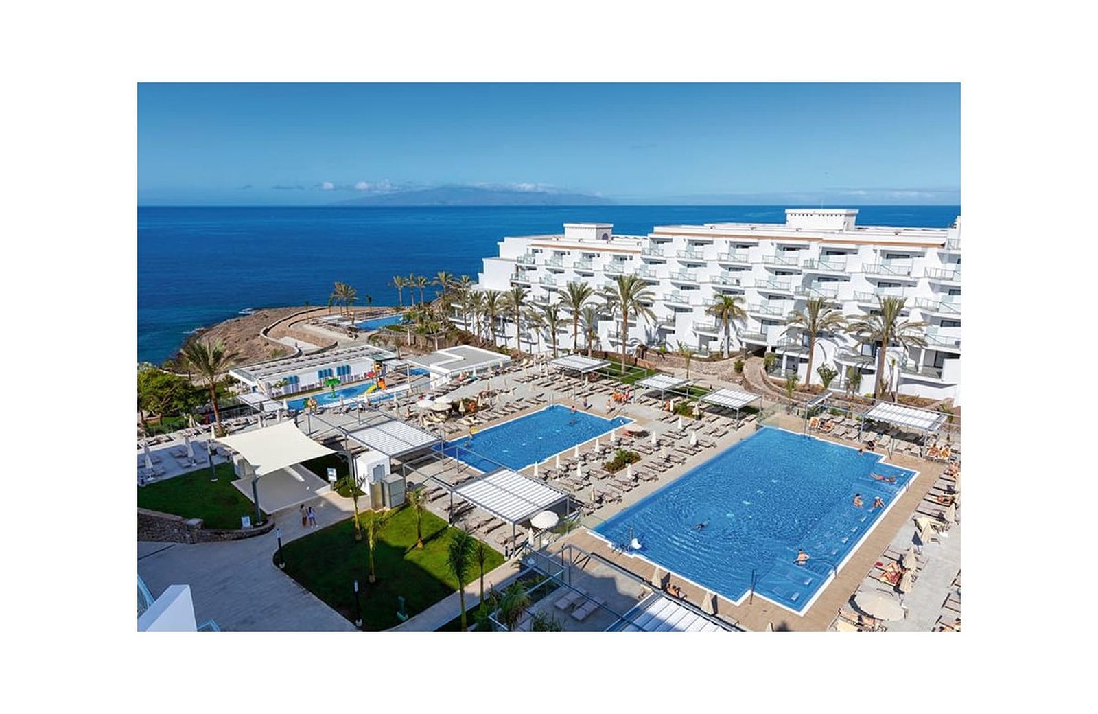 An aerial view of Hotel Riu Buenavista at Playa Paraíso, its guest tower and pools above the coast, with the island of La Gomera on the horizon.