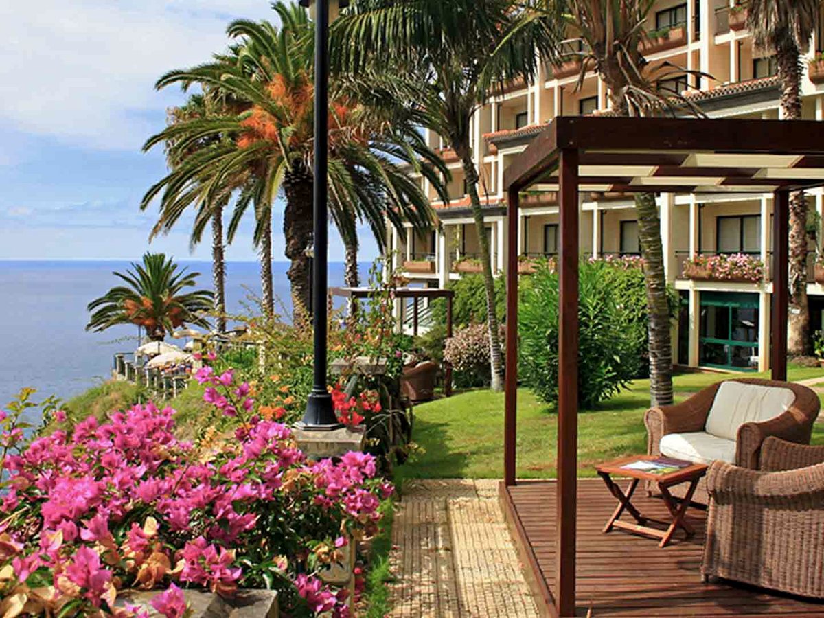 Terraced gardens with bougainvillea, tall palms and a pergola over wicker armchairs, the hotel wing behind and the Atlantic below.