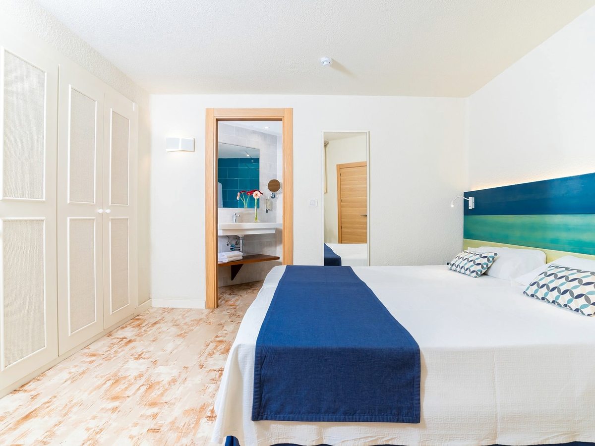 A double bed with a blue runner and fitted wardrobes, an en-suite doorway to one side.