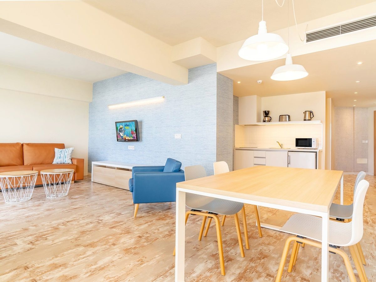 An apartment lounge and dining space with an orange sofa, dining table and a kitchen behind.