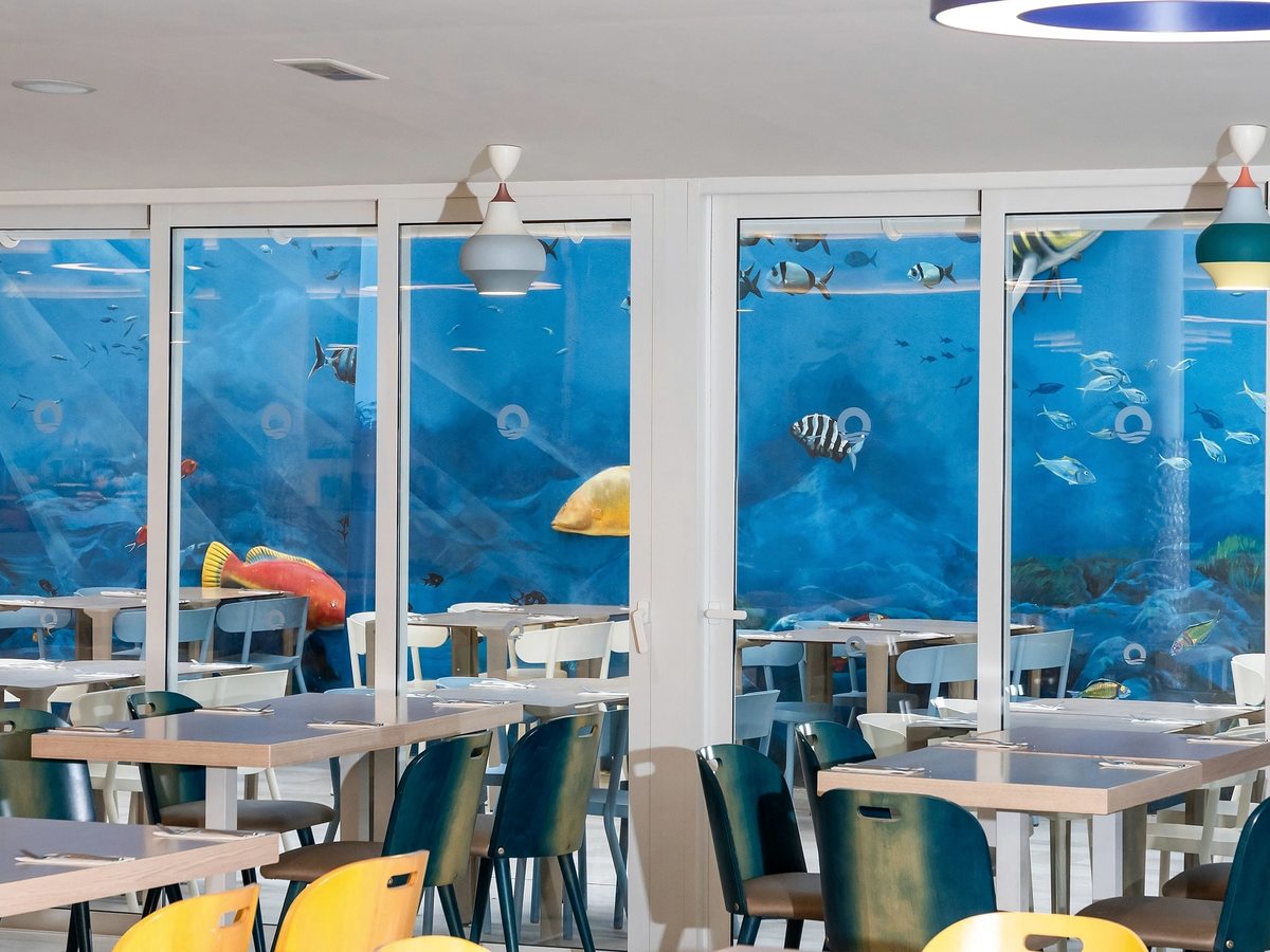 A bright dining room with tables and chairs set in front of blue underwater sea murals.