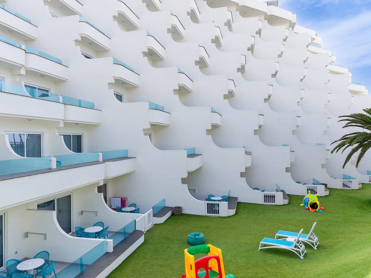 A grassy courtyard with children's play equipment below the hotel's stepped white balconies.