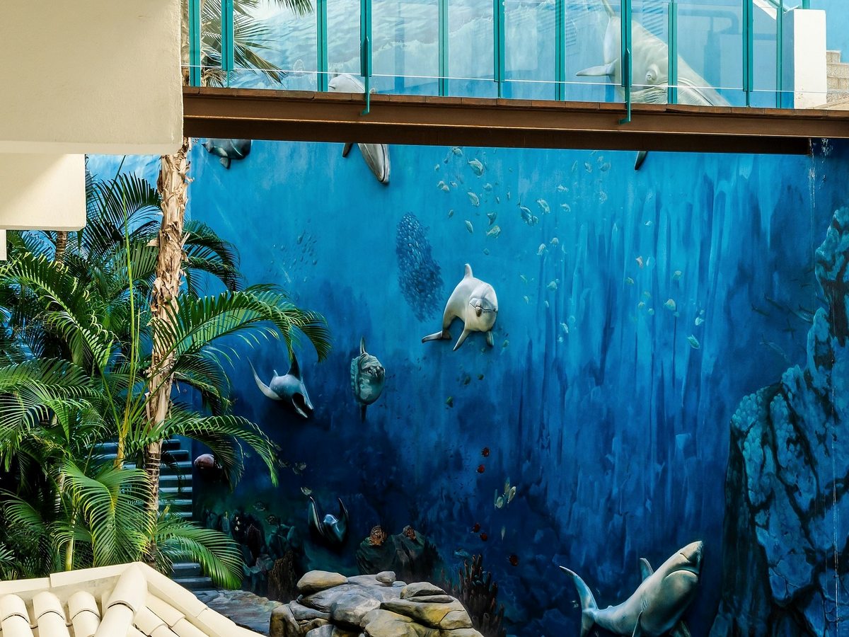 A large blue mural of fish and dolphins beside an elevated glass-sided walkway.