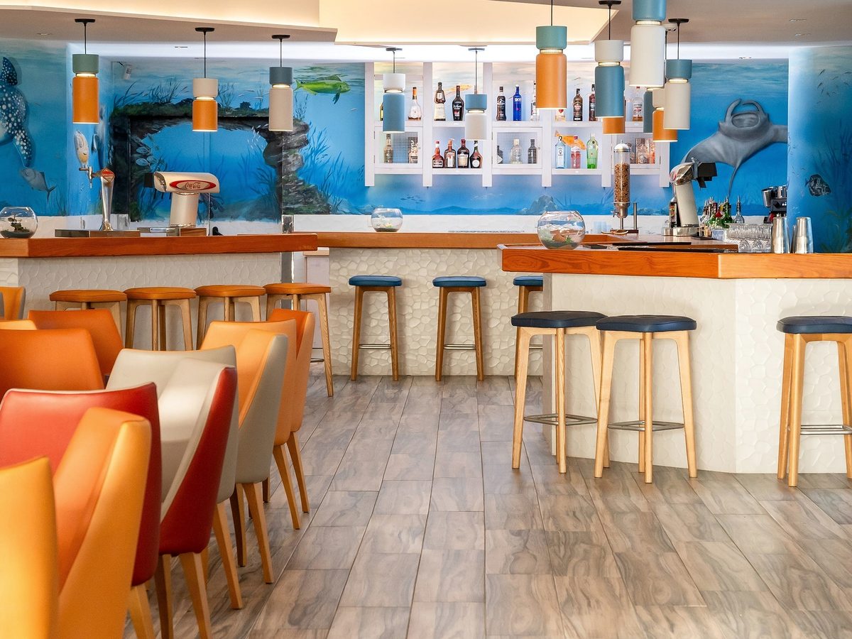 An indoor bar with orange stools along a wooden counter below a marine mural.