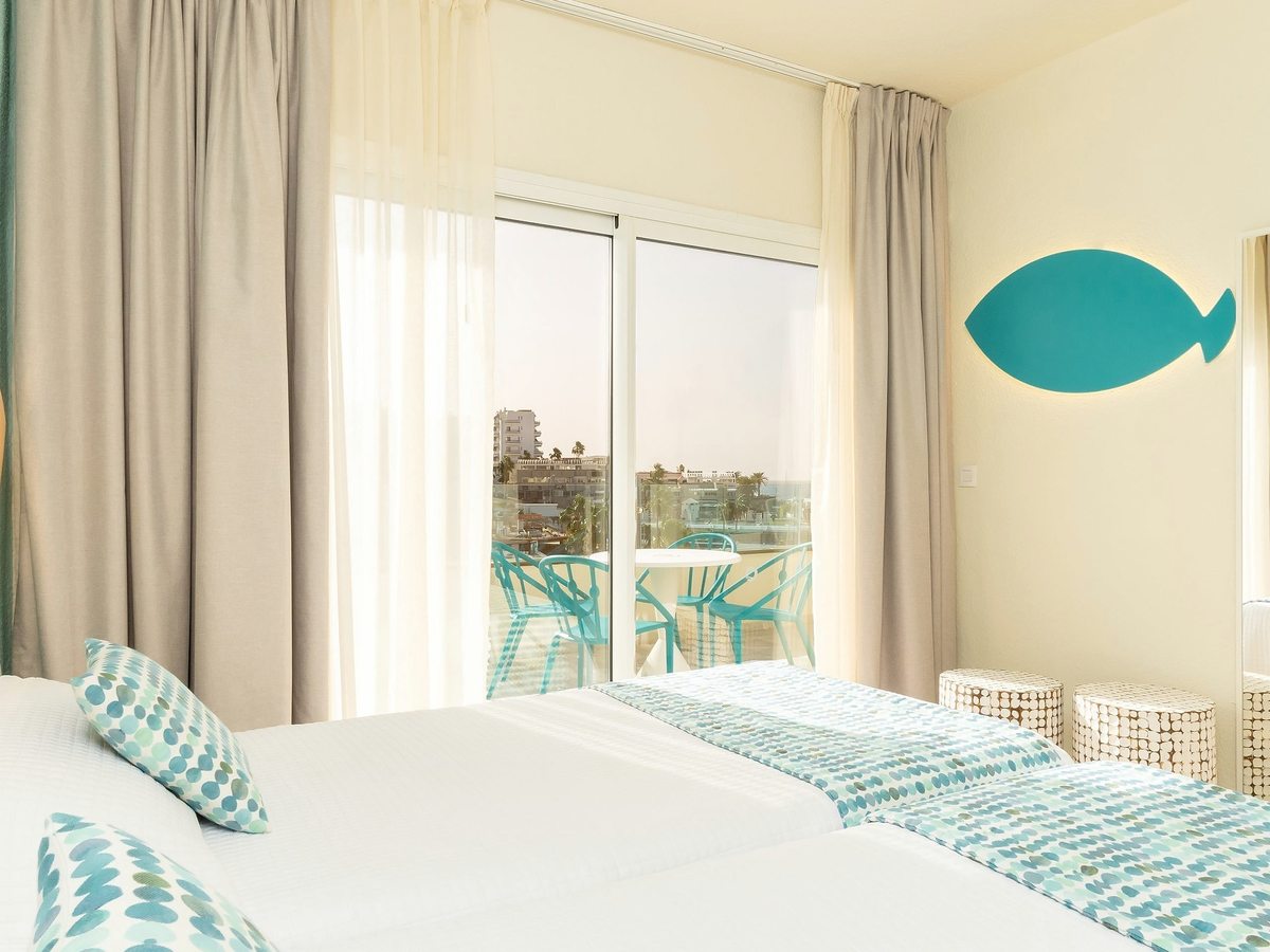 Two single beds with turquoise throws below a fish wall decoration.