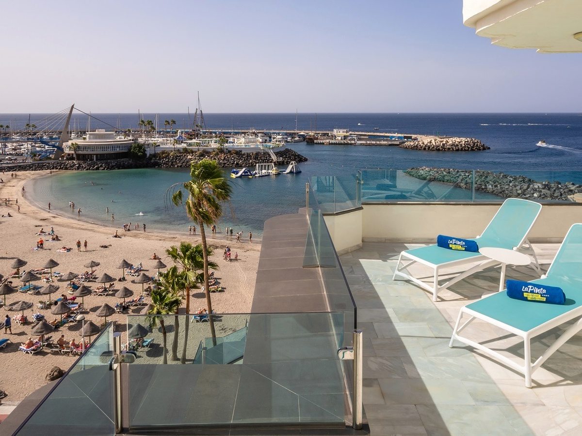 Turquoise loungers on a terrace above the sandy beach and the marina breakwater.