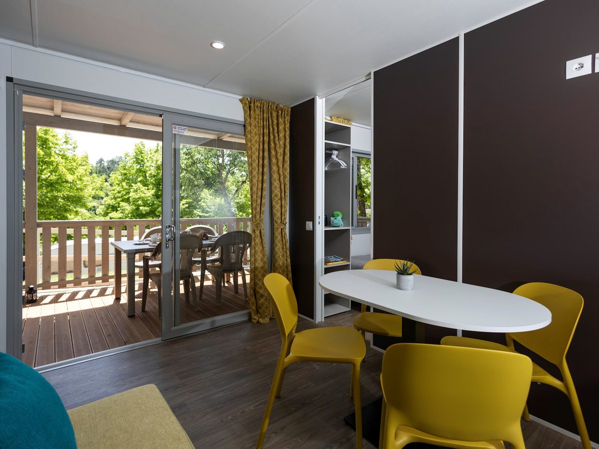 An open-plan interior with a round dining table, yellow chairs and a sofa by a window.