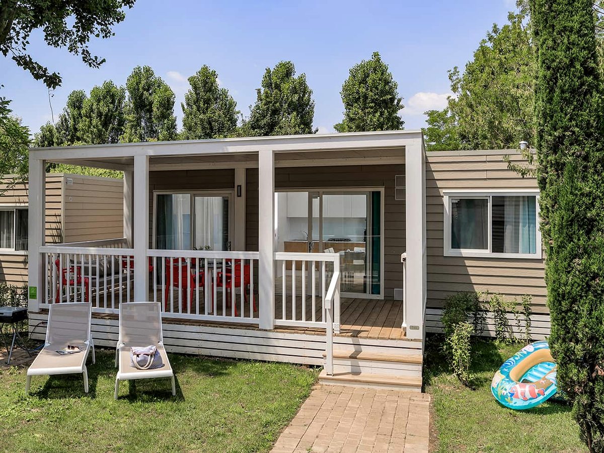Rows of single-storey mobile homes with covered verandas set on grass among tall trees.