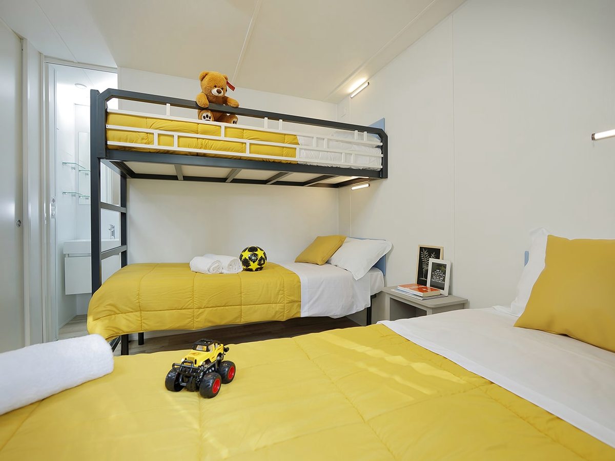 A children's room with a bunk bed and single beds made up with yellow bedding.