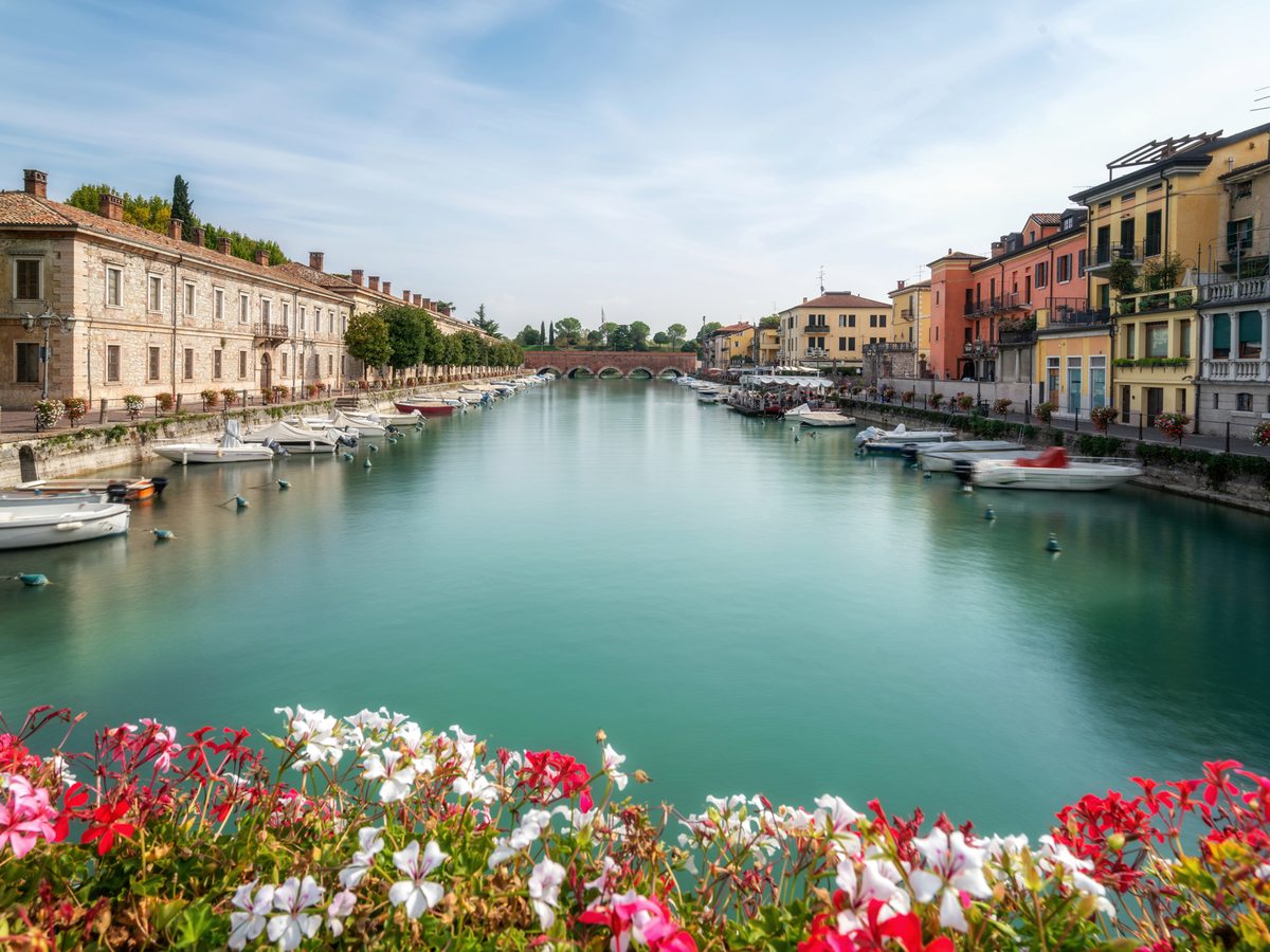 Pastel buildings lining a canal with moored boats in the lakeside town of Peschiera del Garda.