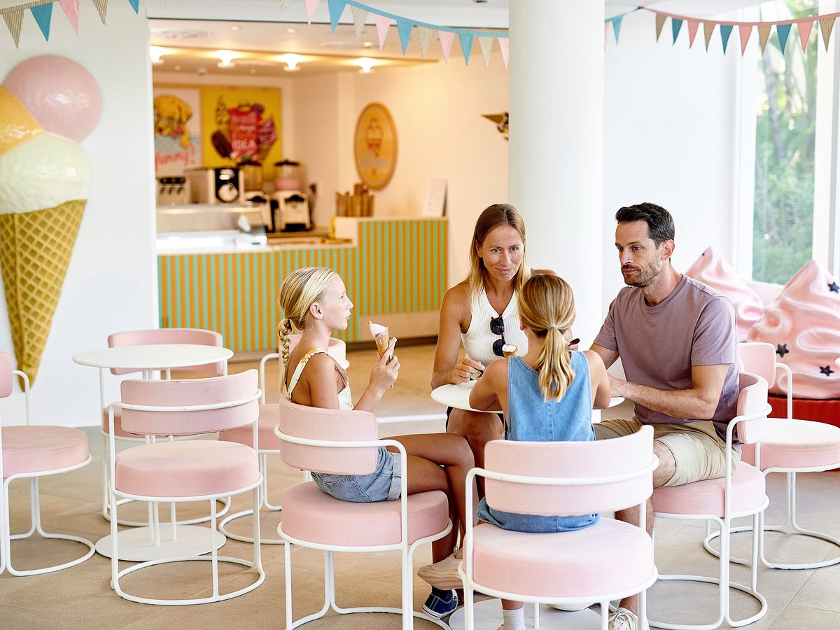 A family eating ice cream at pastel-pink tables in the ice cream parlour, a giant ice-cream-cone decoration on the wall.