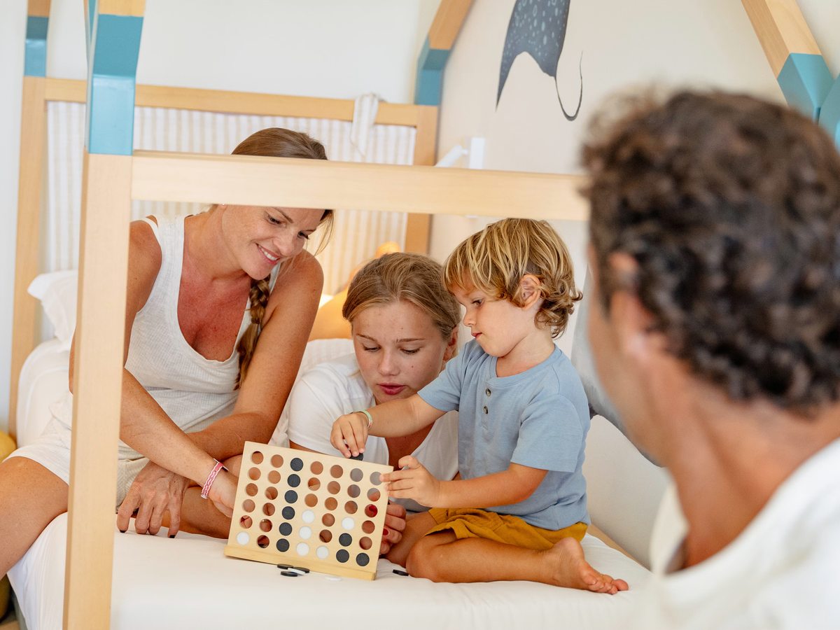 A family sitting on a lower bunk playing a Connect-Four-style game, with sea-creature wall art and a timber bunk frame behind them.