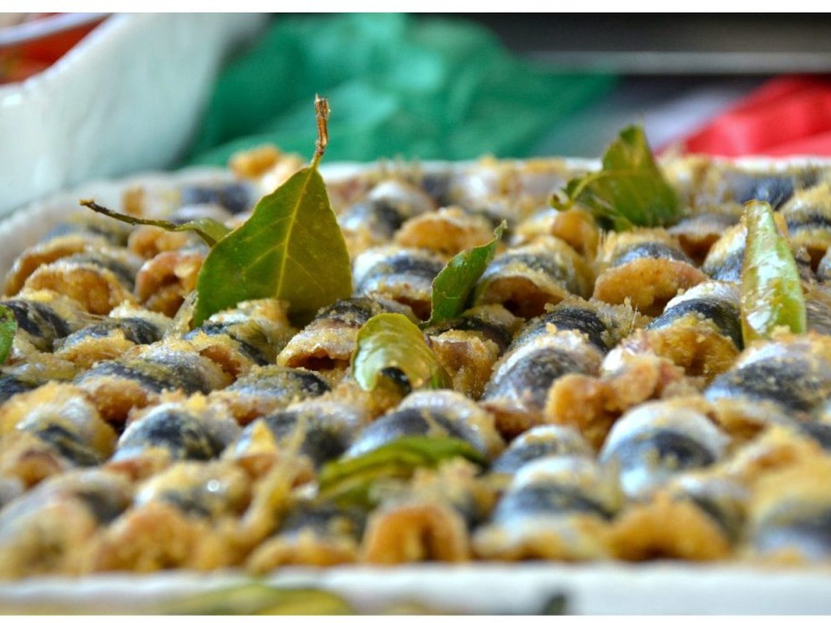 A tray of baked breadcrumbed fish rolls dotted with bay leaves at a buffet.