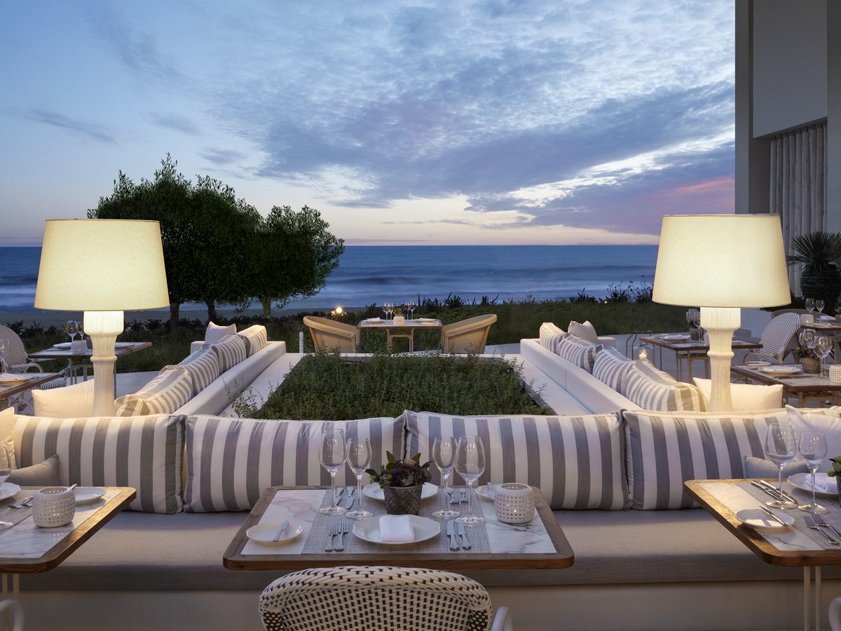 Provence, the French restaurant at Ikos Andalusia, striped banquettes and marble-topped tables on a terrace facing the sea at dusk.