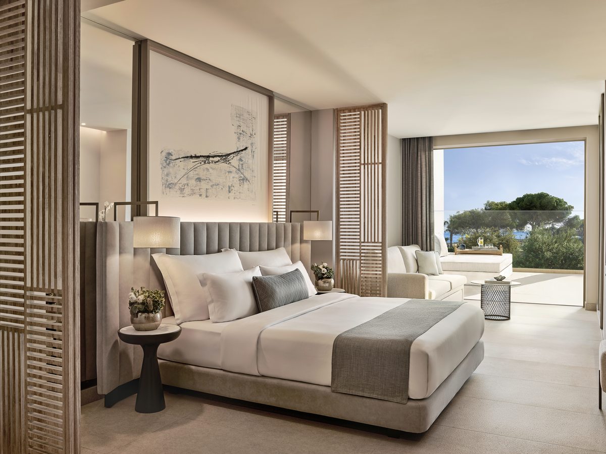 A One Bedroom Suite at Ikos Andalusia, the bed set beside a slatted timber screen with a seating area and the terrace beyond.