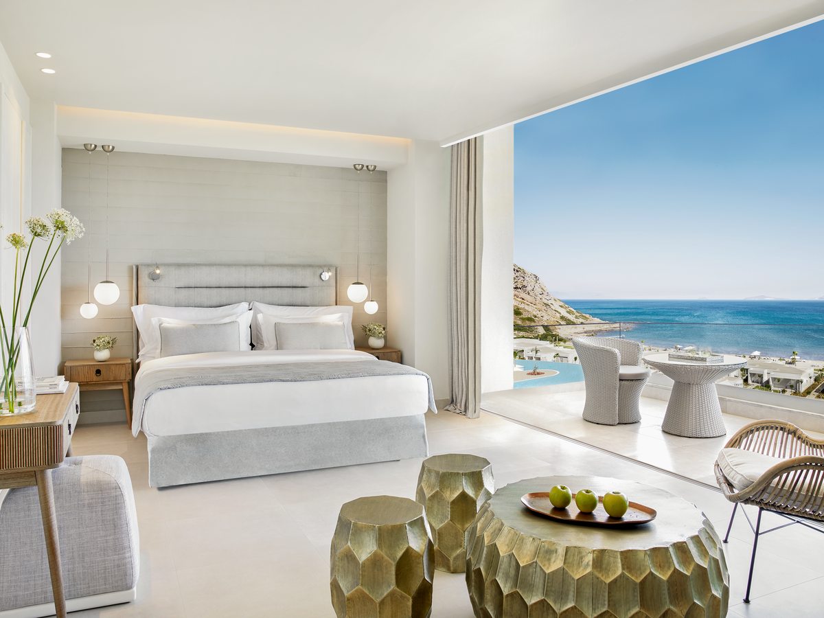 A Panorama Junior Suite, its bed and seating opening through full-height glass to a terrace and the sea.
