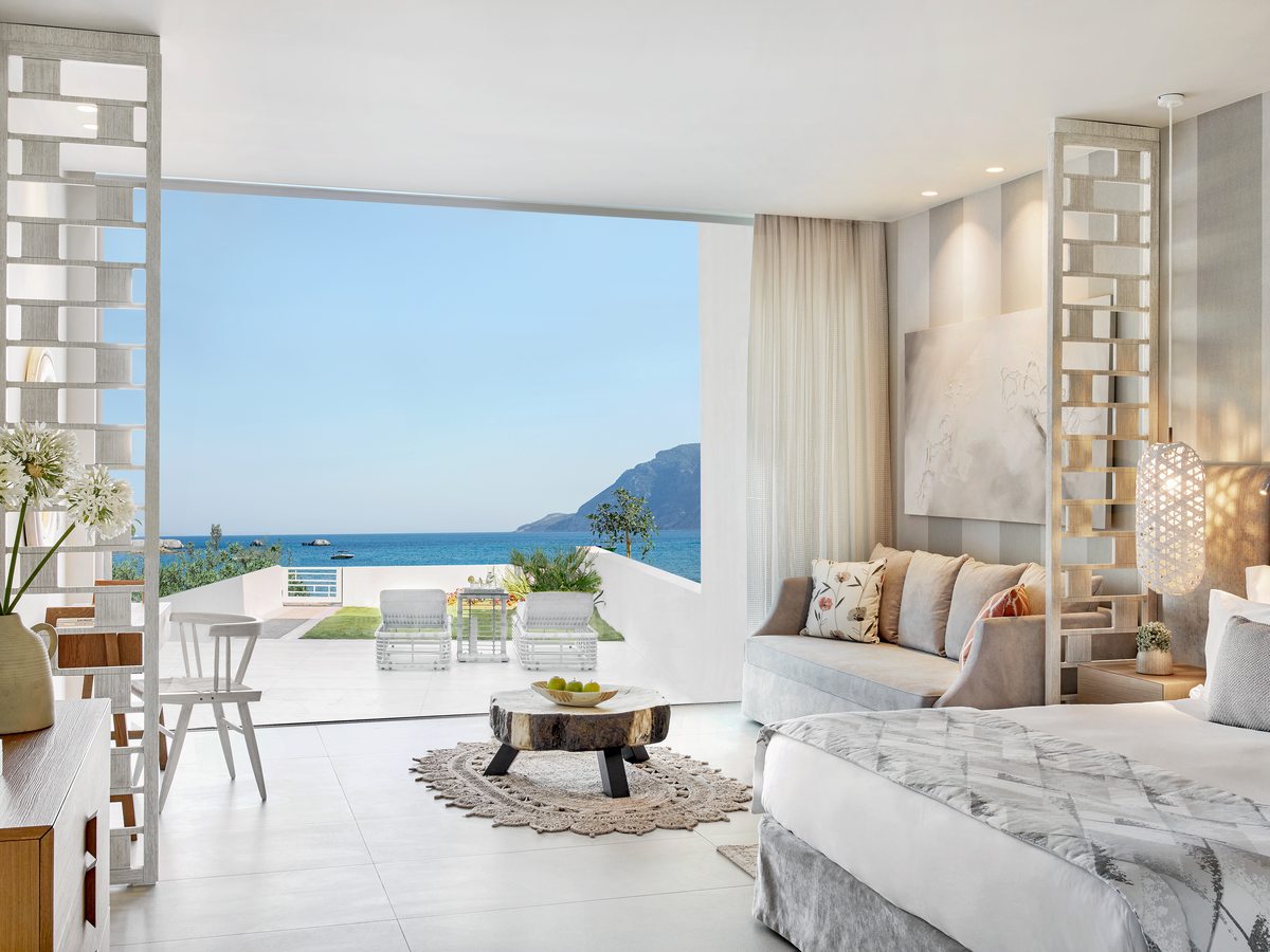 A Deluxe Junior Suite opening to its own garden terrace, with sun loungers on the grass and the sea beyond.
