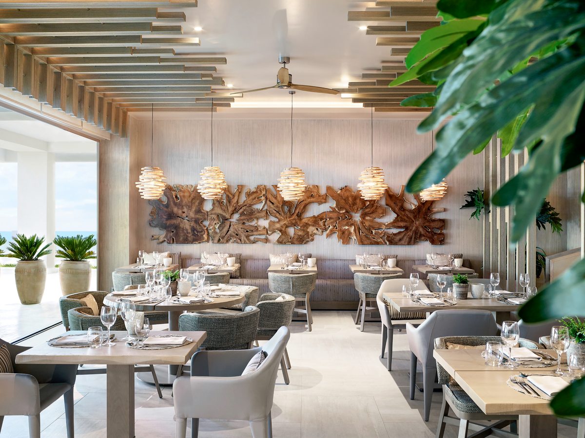 The Flavors dining room, with pale wooden tables under woven pendant lights and a driftwood wall panel along the far wall.