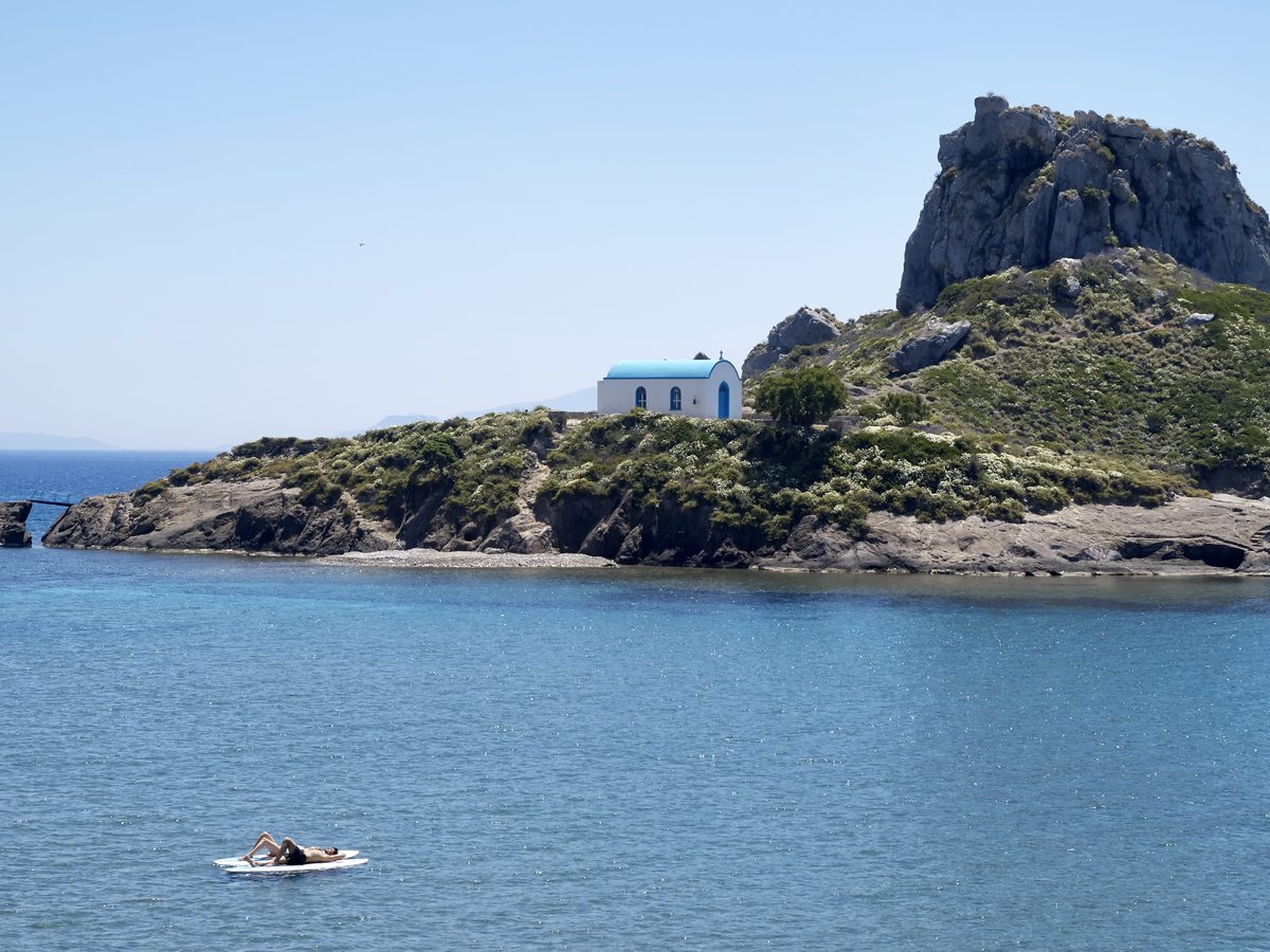 The rocky Kastri islet close up, topped by its small white chapel, with the headland rising behind it.