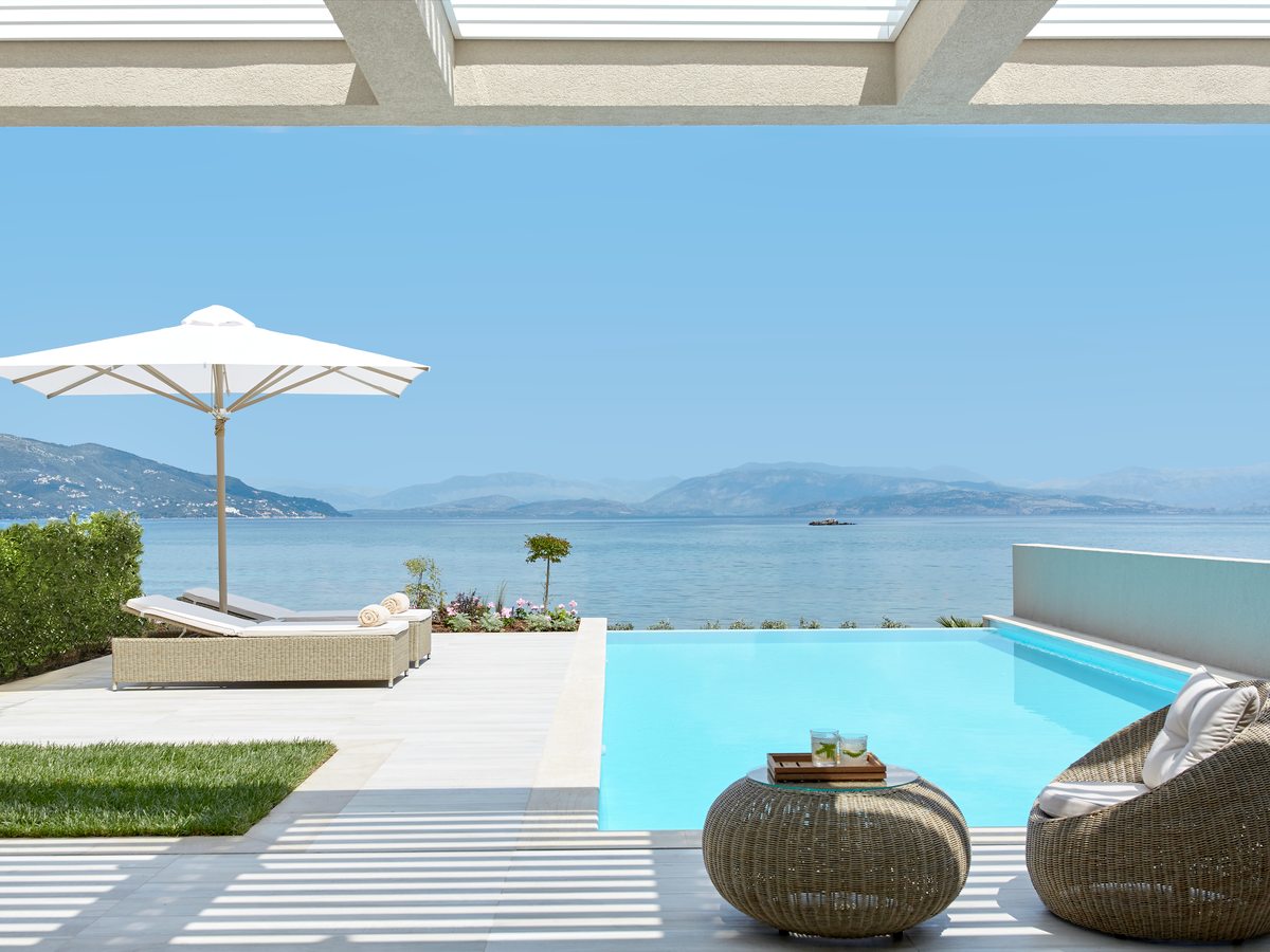 A private pool and sun loungers on a terrace with a parasol, the bay and the hills beyond.