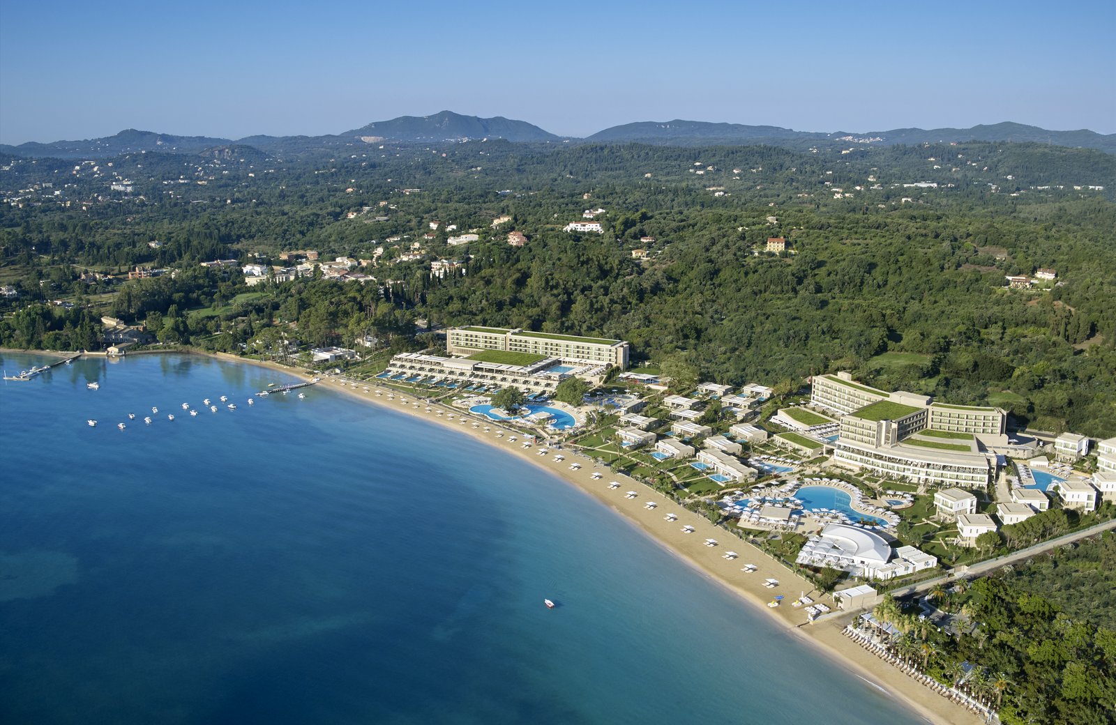 Ikos Dassia from the air: room blocks set among trees on the wooded slopes above a sheltered Corfu bay.