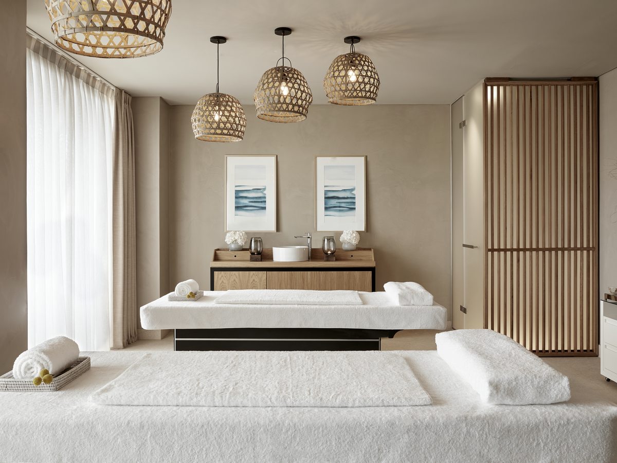 A treatment room at an Ikos spa, with two treatment beds, folded towels and a twin basin unit.