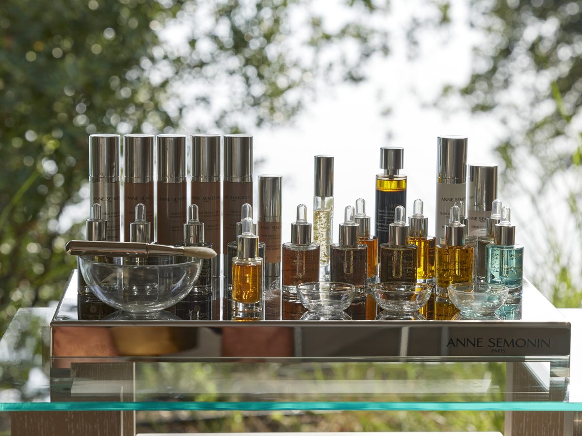 Bottles and droppers of Anne Semonin skincare arranged on a glass trolley under olive trees at an Ikos spa.