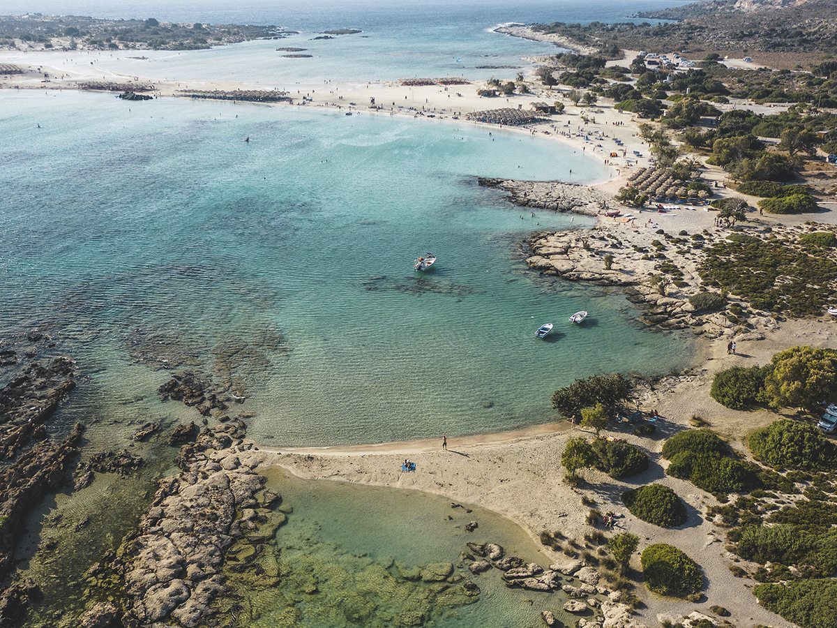 Aerial view of a beach in the far west of Crete near Elafonisi, with sandbars, rocky islets and clear shallow water.