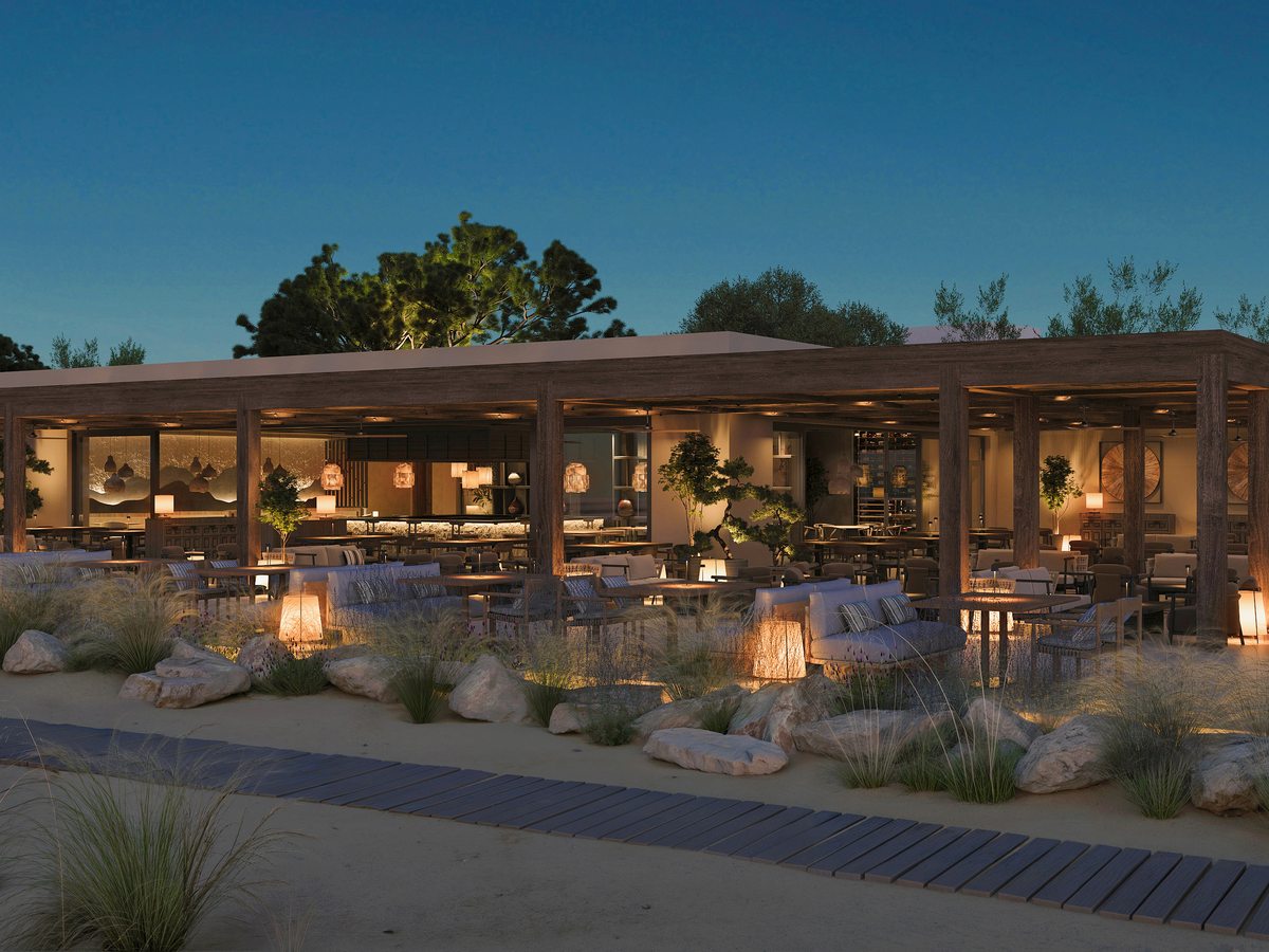 Anaya at Ikos Kissamos, a timber-framed open-sided restaurant lit at dusk, with terrace tables and armchairs set out on the sand in front.
