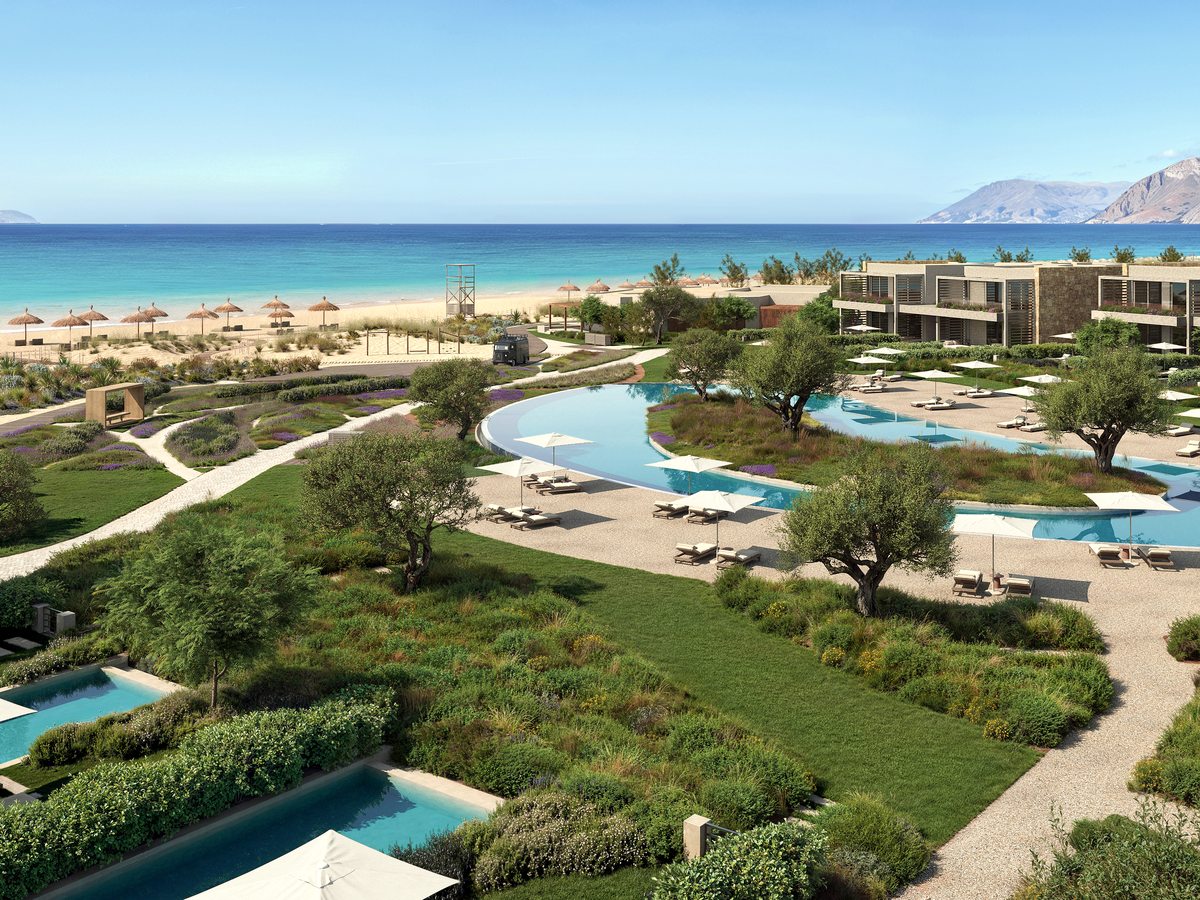 The pools at Ikos Kissamos set among lawns and olive trees, with sunbeds around them and the sandy beach behind.
