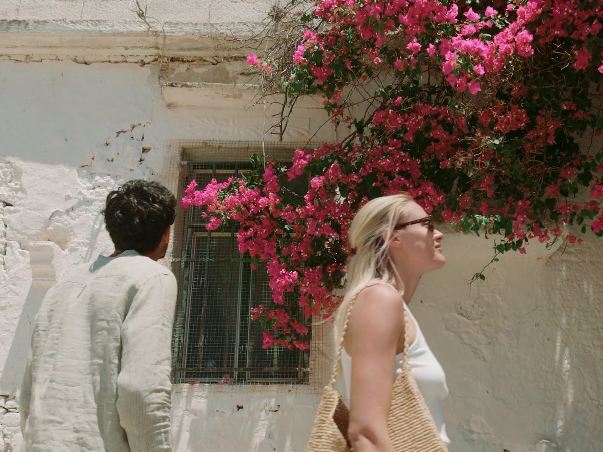 Two people walking past a whitewashed wall hung with bright pink bougainvillea in a Cretan town.