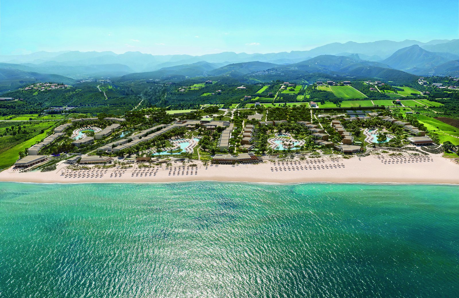 Ikos Kissamos from the air: low room blocks spread along a sandy beach on Kissamos Bay, with the mountains of western Crete behind.