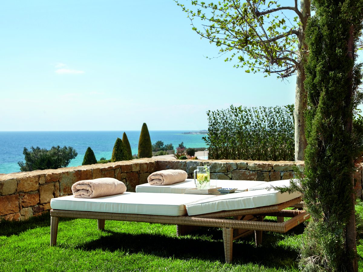 A private garden with a twin sun bed and towels on the lawn, behind a low stone wall with the sea beyond.