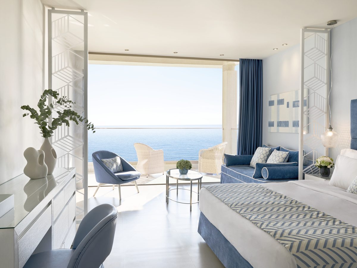 A Panorama Junior Suite with the bed, armchairs and a coffee table in one open space, sliding doors framing the sea.