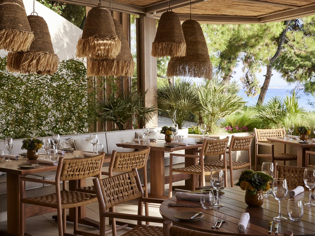 The covered terrace at the Beach Club, with fringed rattan pendants, woven chairs, planting and the sea beyond.
