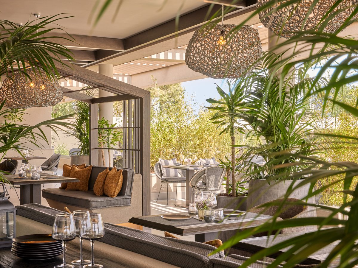 The dining room at Anaya, with a timber counter, woven pendant lights and tall palms by the open windows.