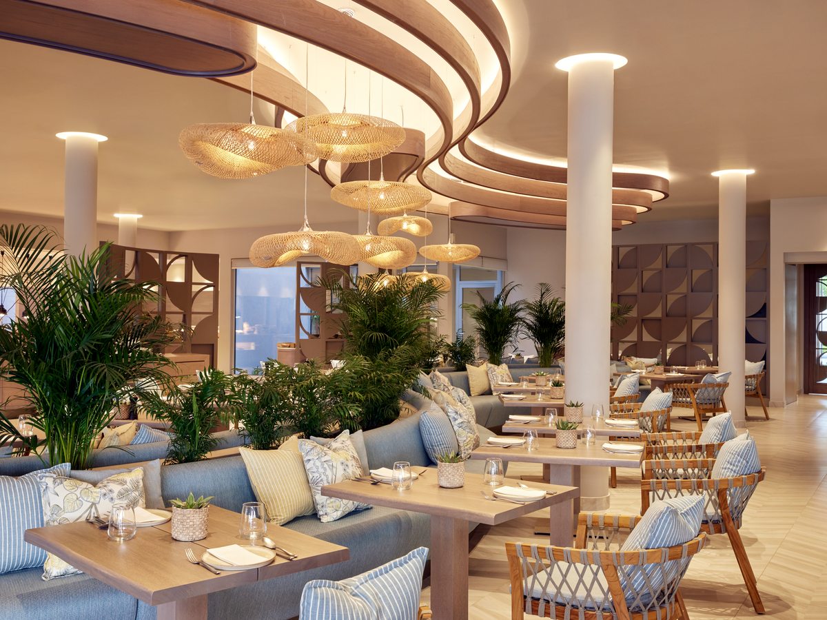 The Flavors dining room with cane chairs, cushioned banquettes and curved pendant lights above set tables.