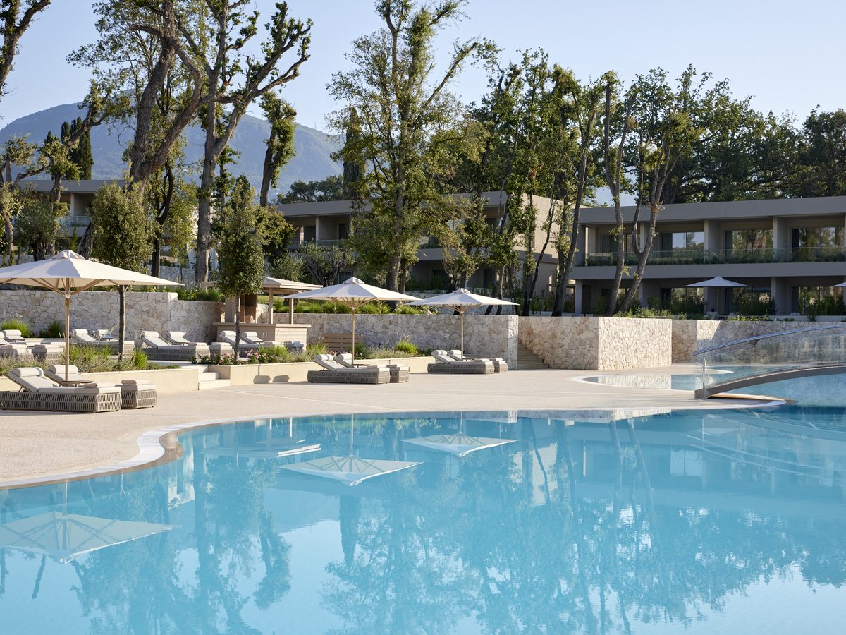 A large freshwater pool with sun loungers and daybeds along its paved surround and the low resort buildings behind.
