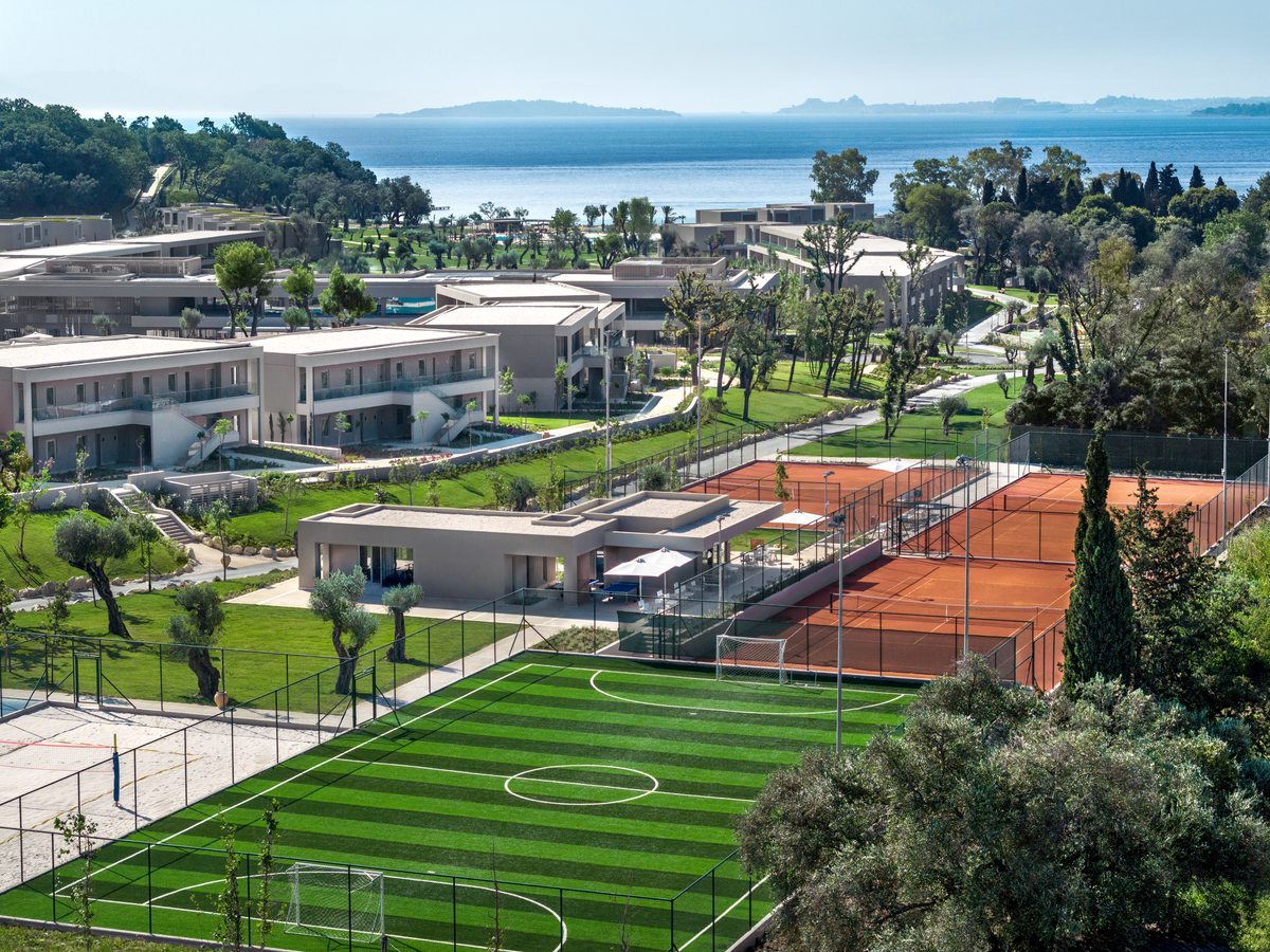 Aerial view of three clay tennis courts and a green football pitch beside the resort buildings and gardens.