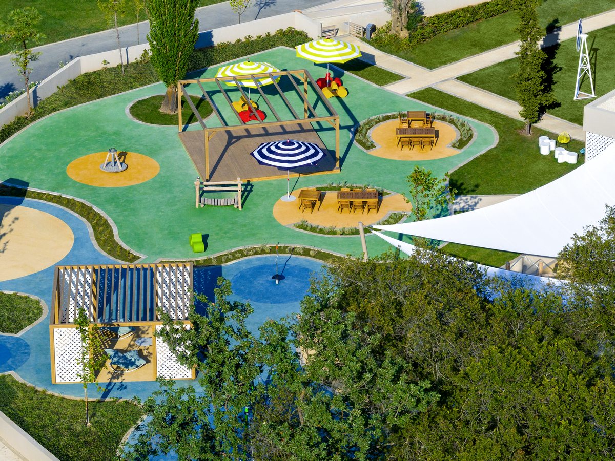 The playground, with climbing frames, slides and shaded seating on soft coloured surfacing among lawns.