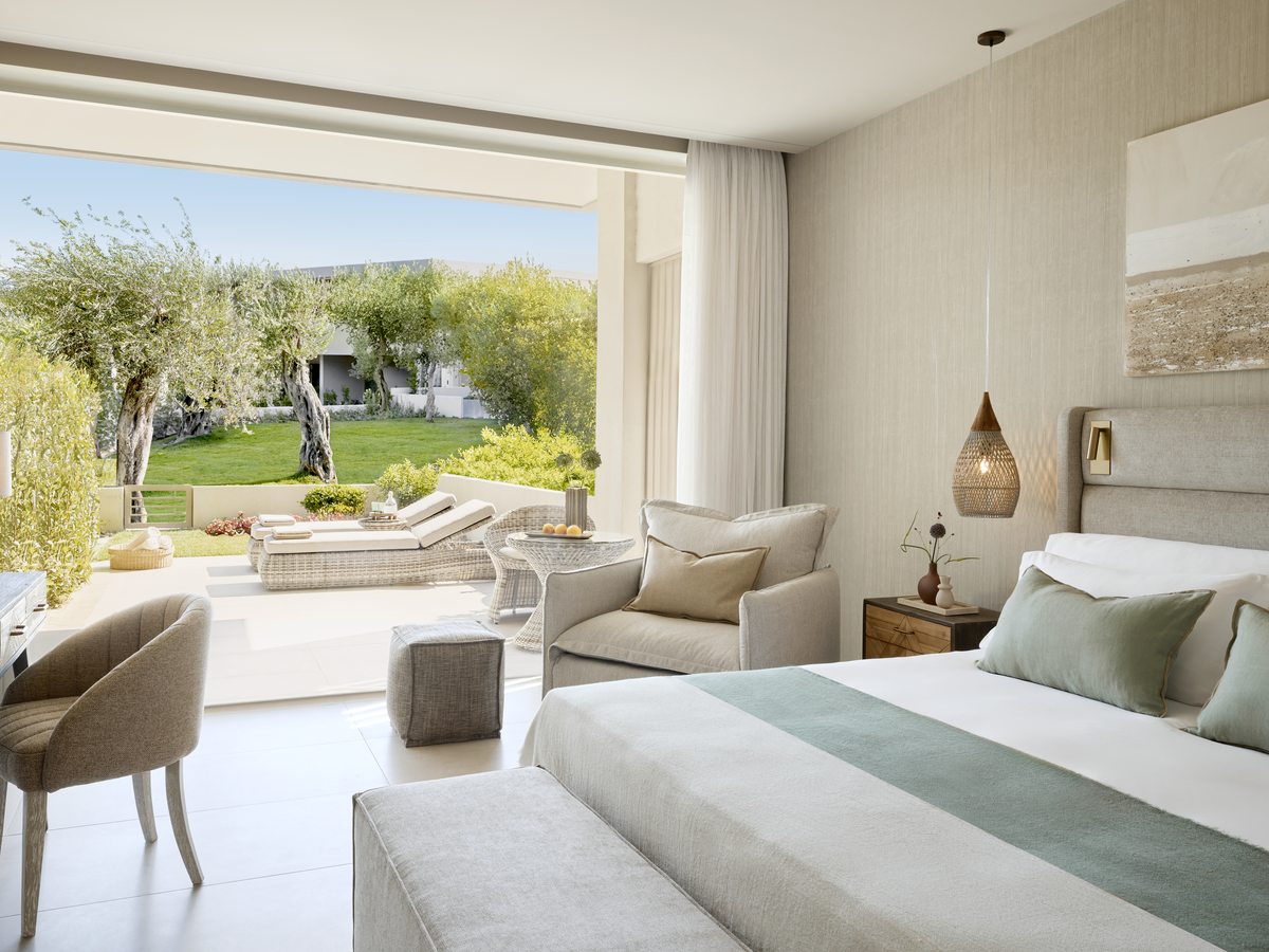 A double bed and armchair in a Superior Double Room, with glass doors open onto a private garden terrace and sun loungers.