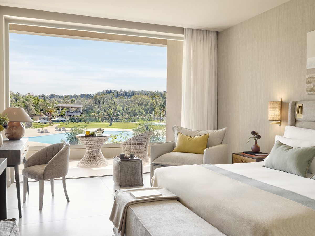 A Family Room with a double bed and a seating area, its doors open to a terrace with the village pool and gardens beyond.
