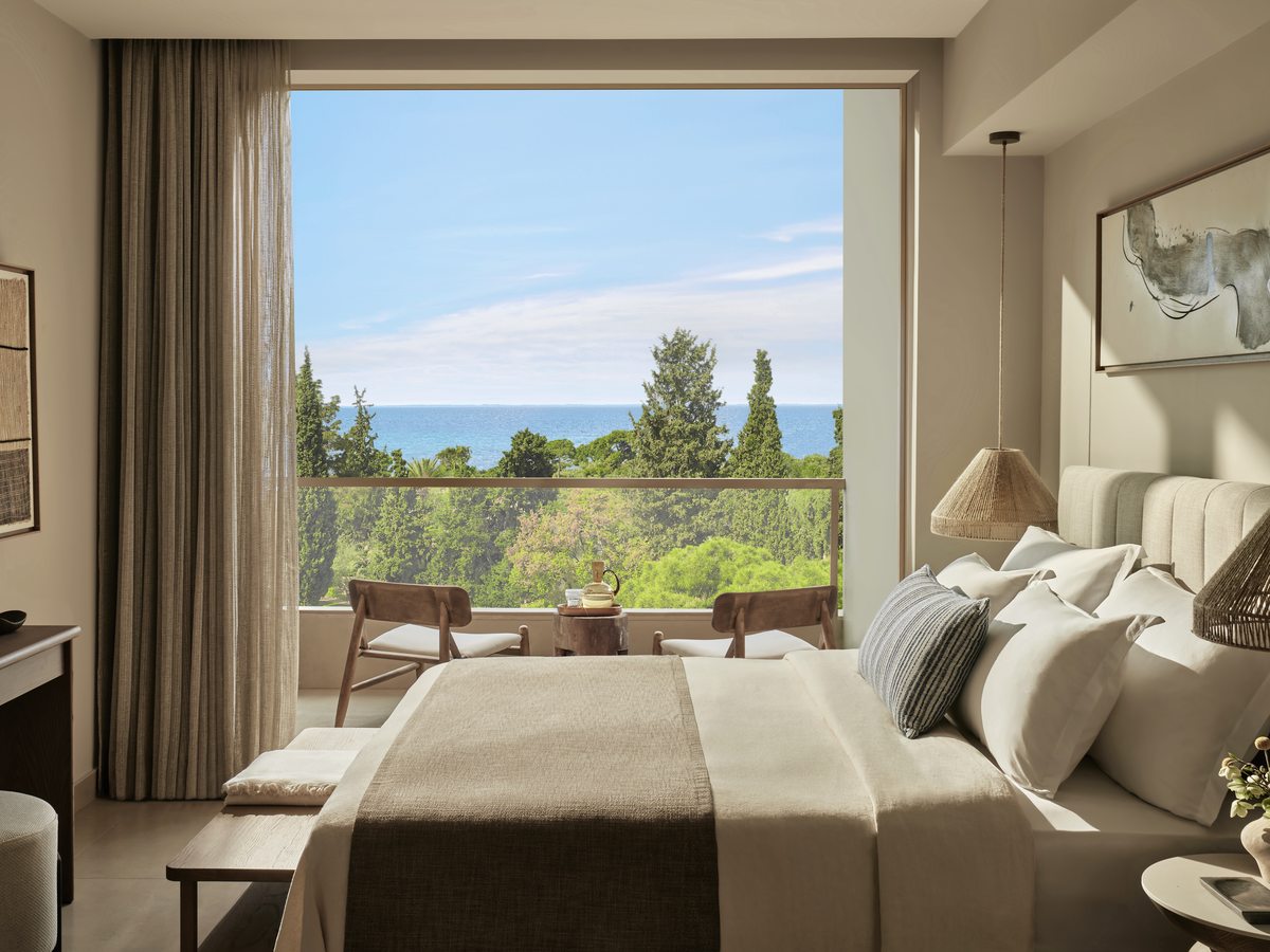 A Superior Double Room with a double bed facing a full-height window over trees and the sea.