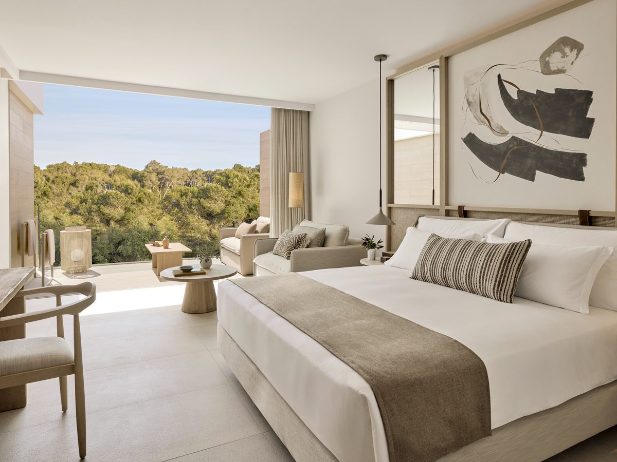 A Superior Double Room with a wide bed, a seating corner and a sliding wall of glass onto a terrace, pines beyond.