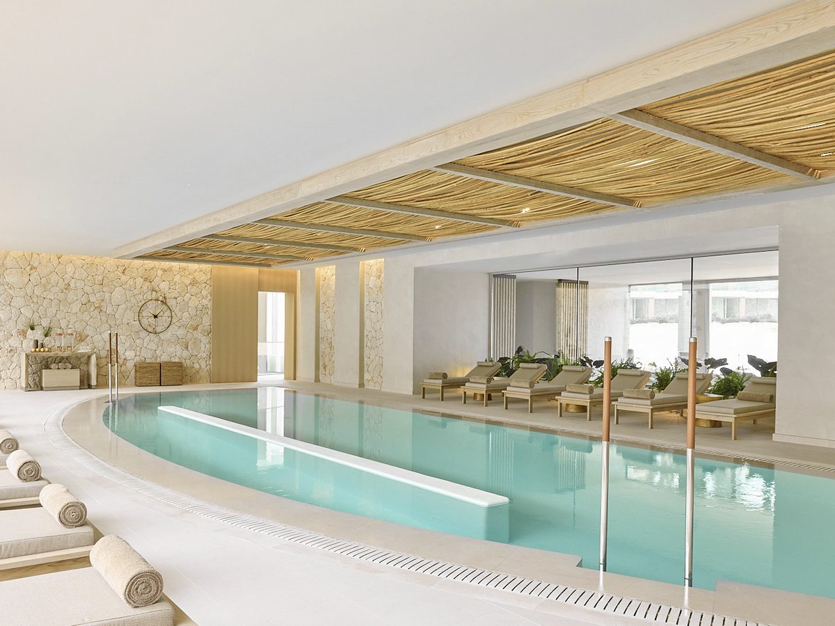 The indoor spa pool under a slatted timber ceiling, with loungers along the far side and a stone wall behind.