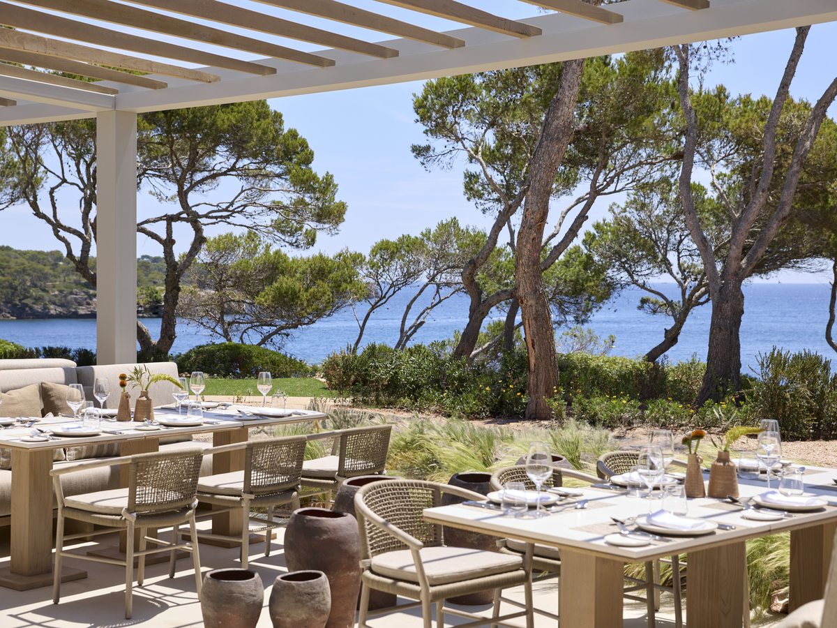 The terrace at Seasons, set tables under a slatted pergola among tall pines, with the sea beyond.