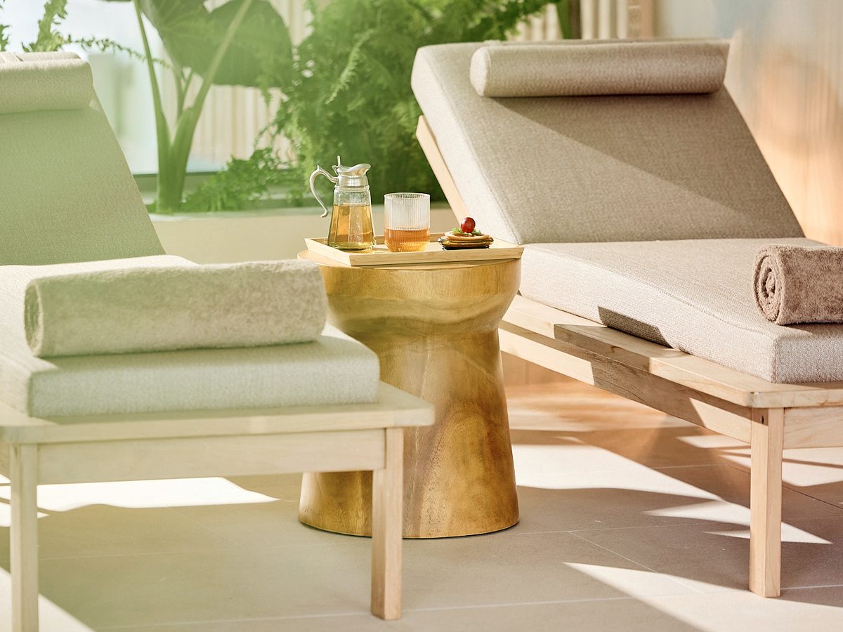 Cushioned loungers in the spa relaxation area, with rolled towels on them and a tray of tea on a side table, and plants behind.