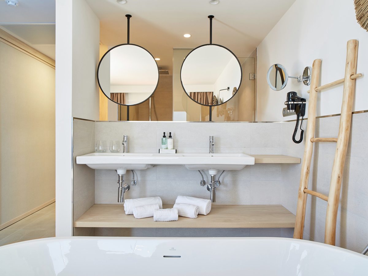 A bathroom with twin basins, round mirrors, a ladder towel rail and a freestanding bath.
