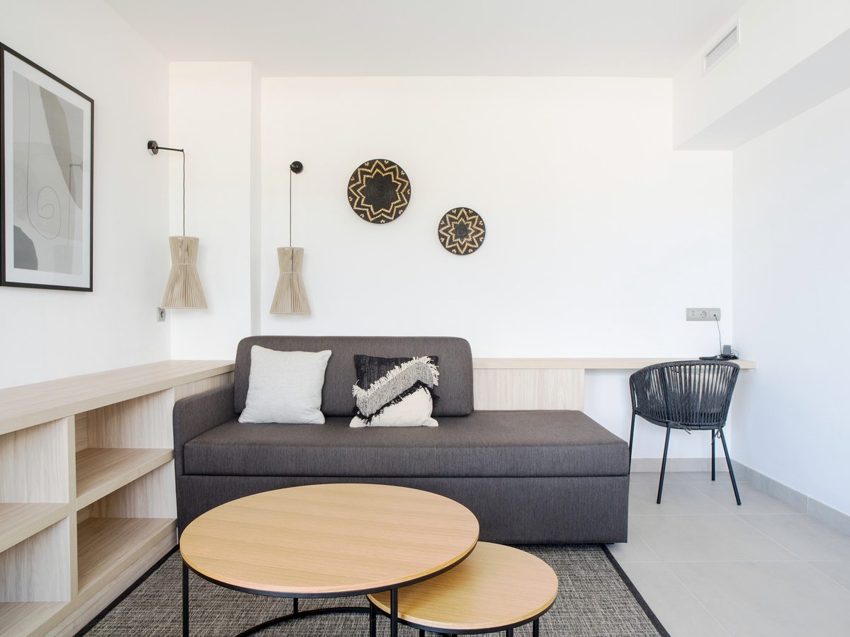 A suite living area with a dark sofa bed, a built-in desk and open shelving.